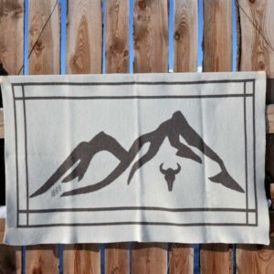 The 1889 Limited Edition Montana blanket hanging from a wooden fence showing the woven Montana mountains and cow skull.