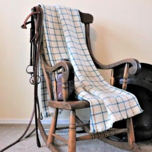 Our latitude blanket with a blue grid line pattern draped over the back of a wooden rocking chair.