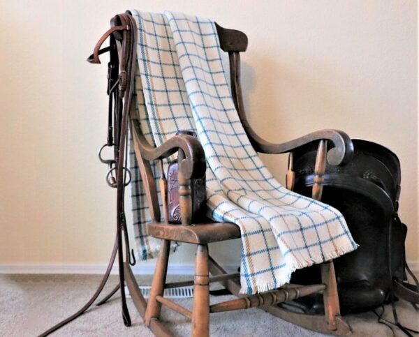Our latitude blanket with a blue grid line pattern draped over the back of a wooden rocking chair.