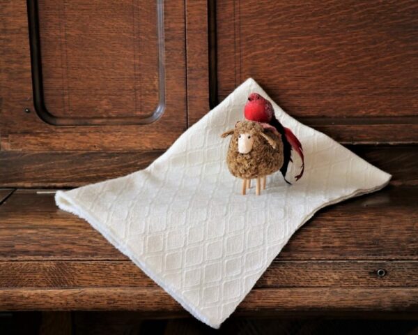 Yogo baby blanket, white with sapphire weave design, draped over furniture with a tiny lamb figurine perched on top.