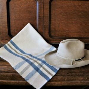 Baby blanket with a blue cross-weave pattern folded and resting on a piece of furniture with a cowboy hat placed on top.