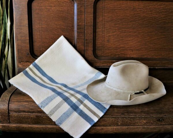 Baby blanket with a blue cross-weave pattern folded and resting on a piece of furniture with a cowboy hat placed on top.